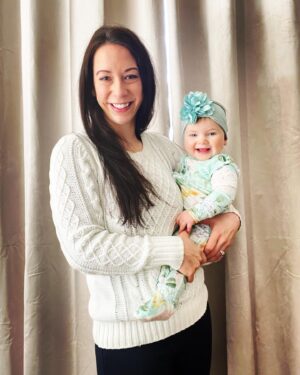 Young 30s mom holding baby girl in blue flowered onesie and teal flowered headband with flower