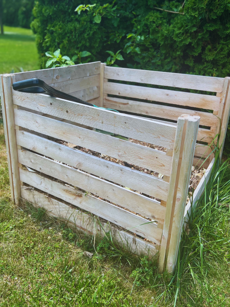 Wood compost bin with green grass and trees on homestead