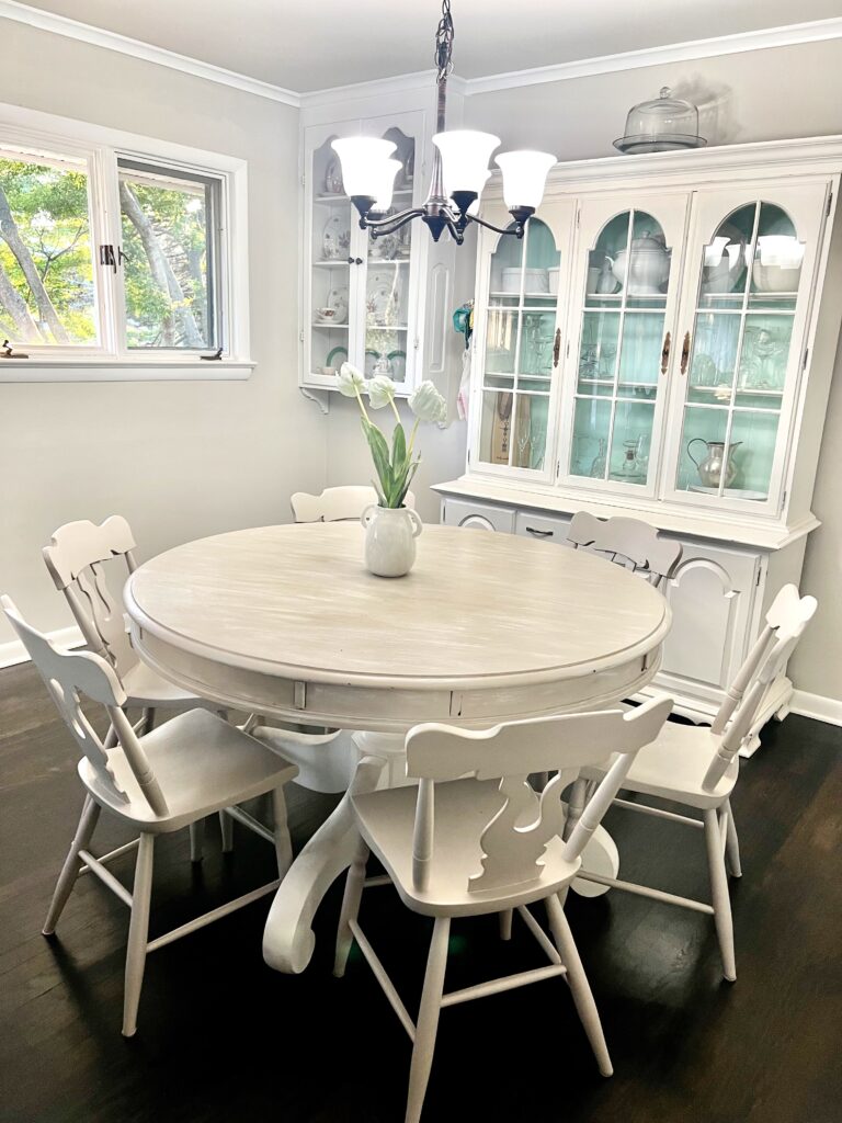 neutral painted dining table and neutral wood chairs in front of china cabinets